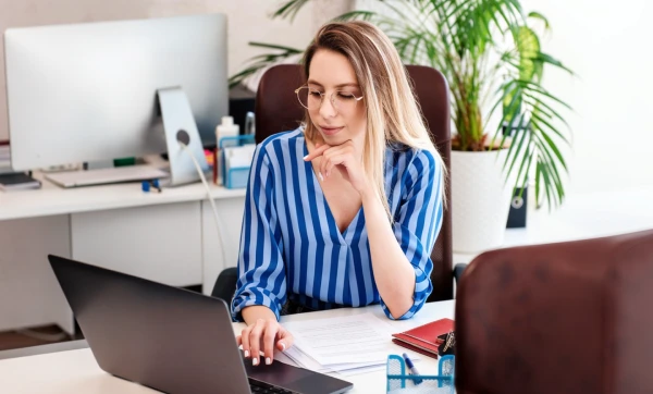 Mulher empresária trabalhando em seu notebook sobre uma mesa em ambiente de escritório sobre Como contratos impactam retenção de tributos.
