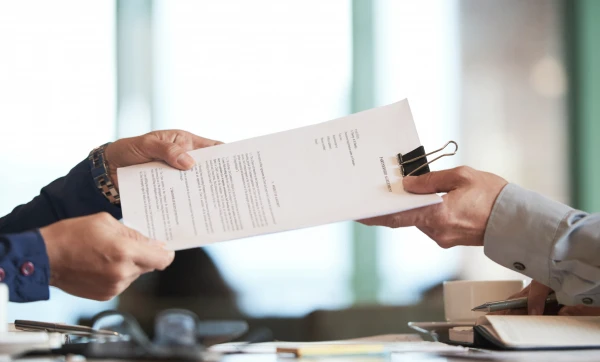 Dois homens profissionais entregando documento de distrato um para outro representando: Distrato comercial: como formalizar o cancelamento de um contrato de prestação de serviços