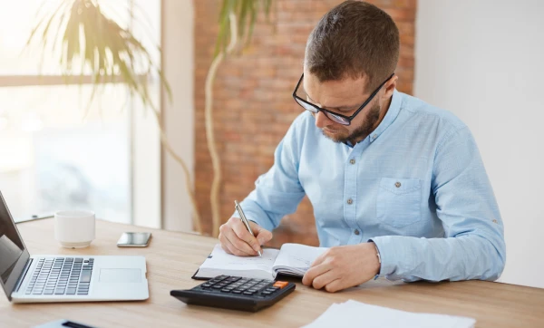 Empresário sentado em sua mesa de escritórios fazendo calculos em um papel, representando: Execução fiscal contra microempresa: o que acontece quando a dívida tributária vai para o judiciário