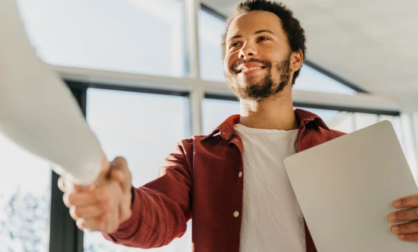 Trabalhador sorridente com um documento em mãos dando um aperto de mão, representando: Como contratar o primeiro funcionário: passo a passo para MEI e ME